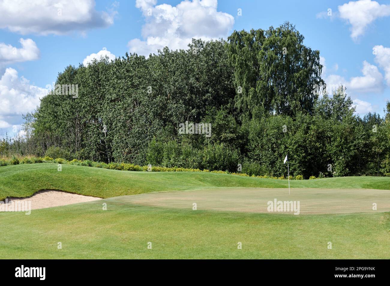 Ein sonnenbeleuchtetes Hintergrundbild eines grünen Golfplatzes mit blauem Himmel und ohne Menschen Stockfoto
