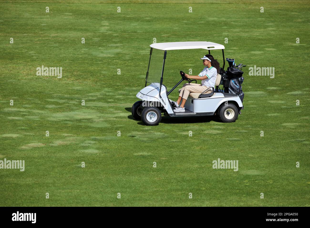 Großer Blickwinkel auf eine junge Frau, die einen Golfwagen auf einem grünen Feld im Sonnenlicht fährt, Kopierraum Stockfoto