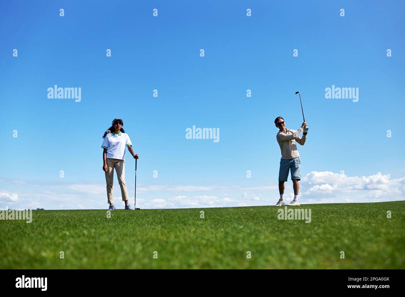 Porträt des aktiven sportlichen Paares, das Golf auf dem Spielfeld gegen den blauen Himmel spielt, Kopierraum Stockfoto