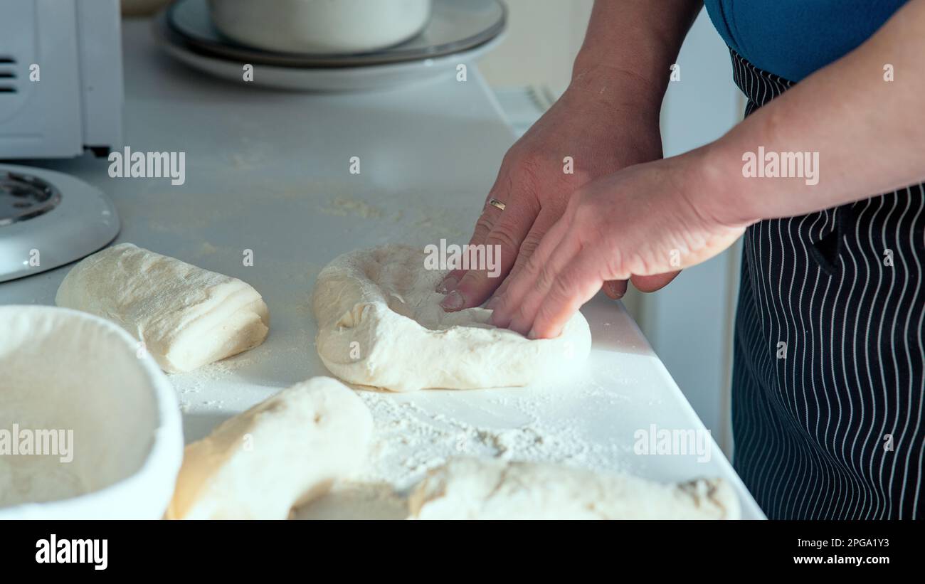 Männlicher Koch macht hausgemachtes Brot auf weißem Tisch. Der Koch streckt und faltet Brotteig auf dem weißen Tisch mit Blick auf das staubige Mehl. Stockfoto