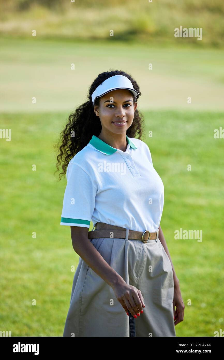 Vertikales Porträt einer lächelnden schwarzen Frau, die draußen Golf spielt und Aktivkleidung trägt Stockfoto
