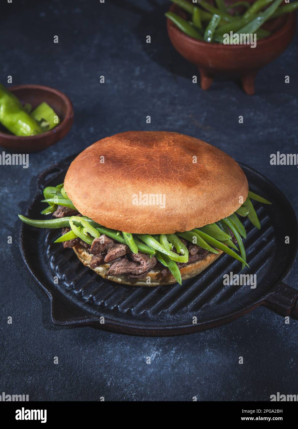 Chilenischer lateinamerikanischer Sandwich-Burger Chacarero mit hochwertigen Rinderschnitten und grünen Bohnen auf schwarzem Hintergrund. Stockfoto