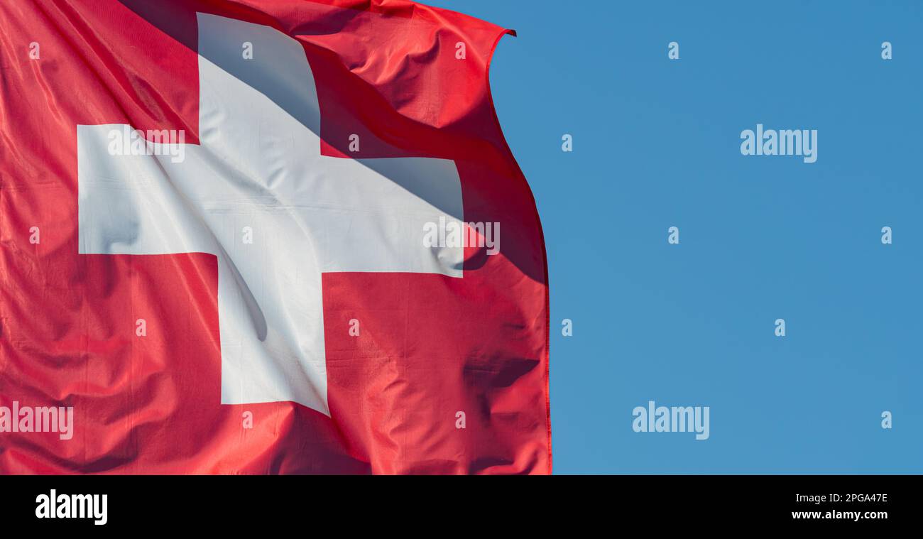 Schweizer Flagge. Schweizer Flagge gegen blauen Himmel. Eine rote quadratische Flagge mit einem weißen Kreuz in der Mitte. Objekte. Stockfoto