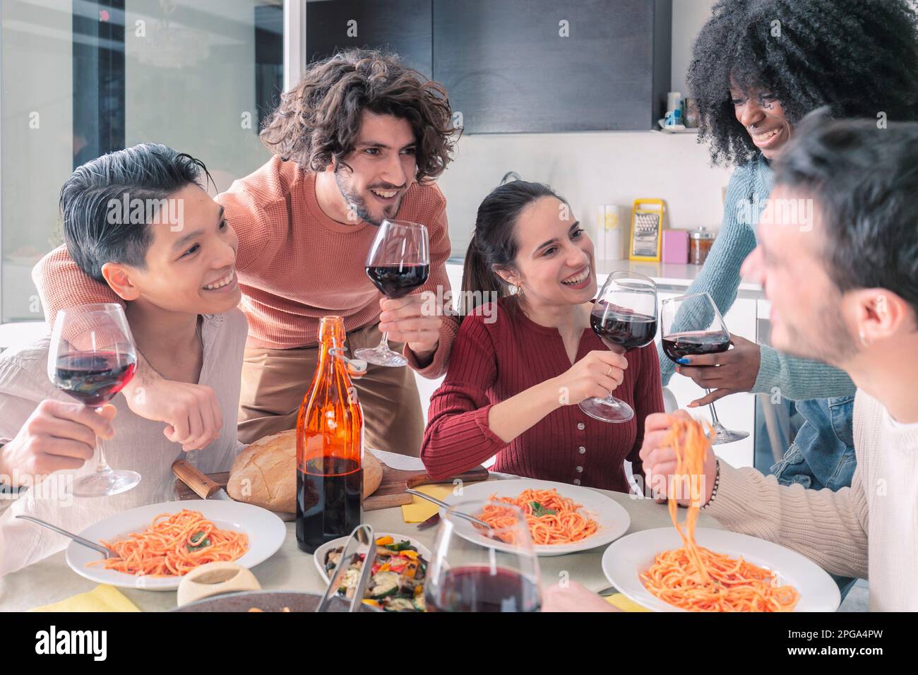 Multiethnische Freunde, die zu Hause Pasta essen und Wein trinken Stockfoto