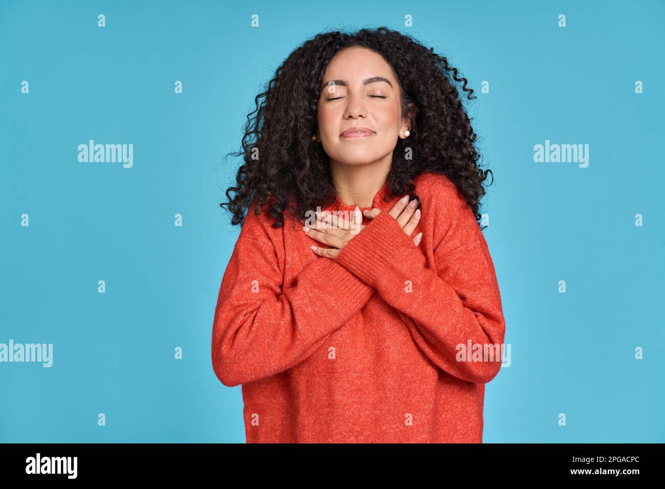 Glückliche latina, die Hände an der Brust hält und Dankbarkeit ausdrückt, isoliert auf Blau. Stockfoto