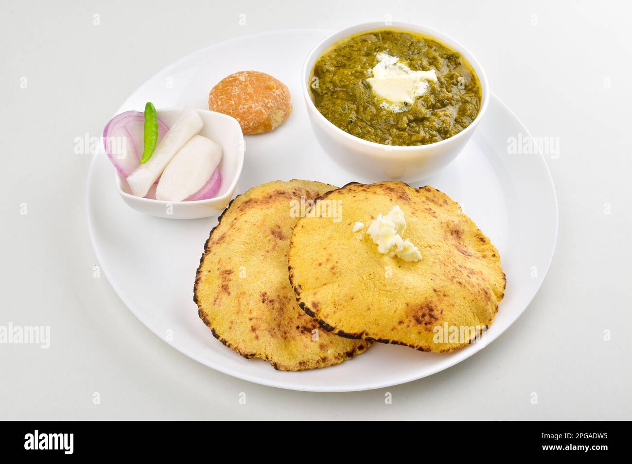 Saag mit Roti serviert mit Jaggery und Salat auf einem Teller isoliert auf weißem Hintergrund Stockfoto