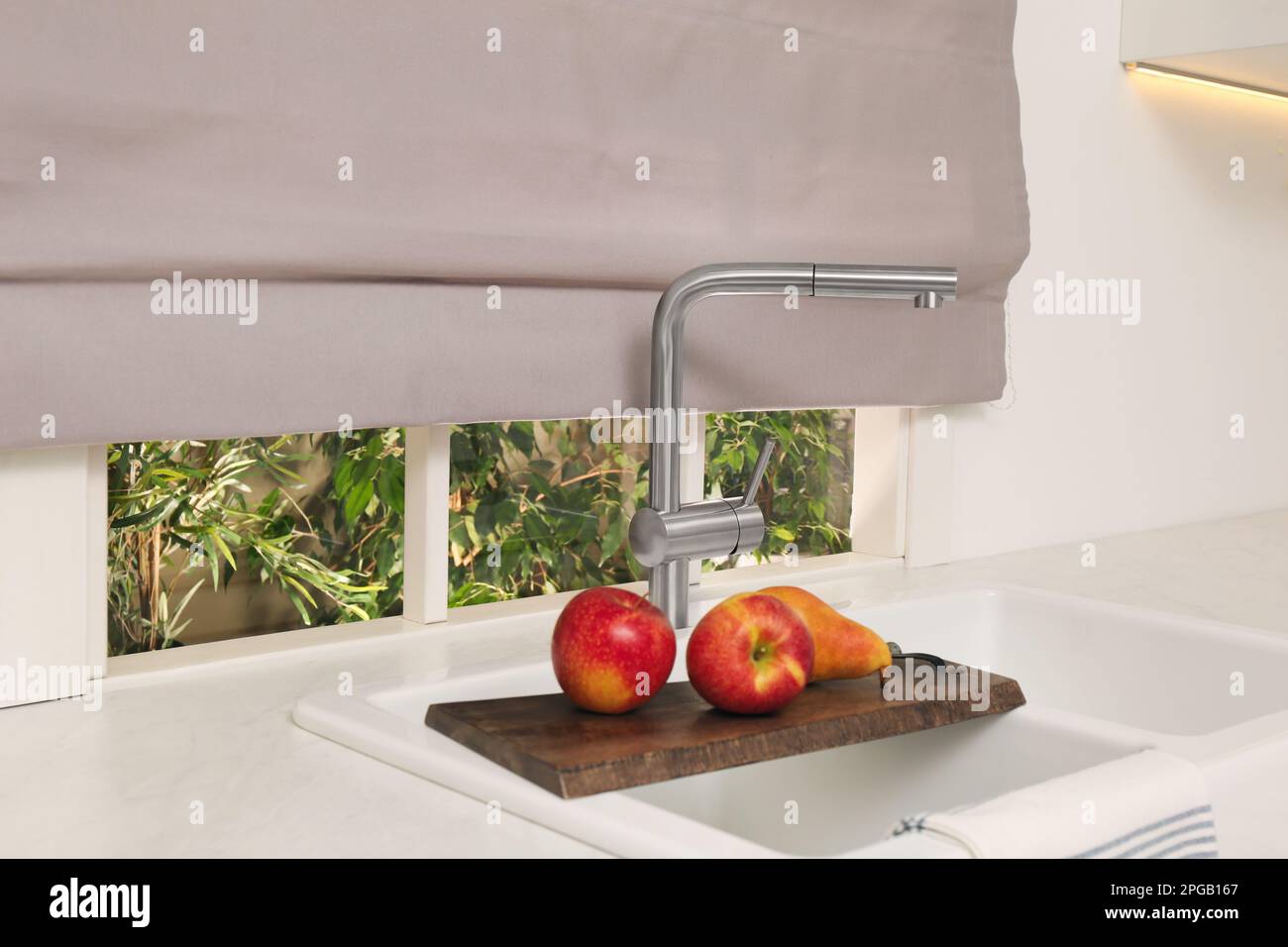 Weiße Doppelschüssel, Küchenspüle mit Holzbrett und frischem Obst vor dem Fenster Stockfoto