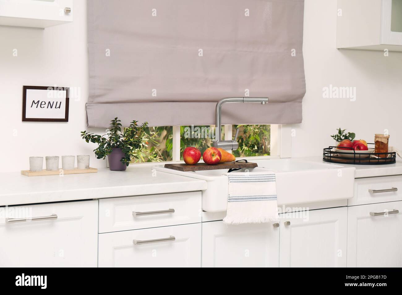 Weiße Küche mit Doppelwaschbecken vor dem Fenster und frischem Obst Stockfoto