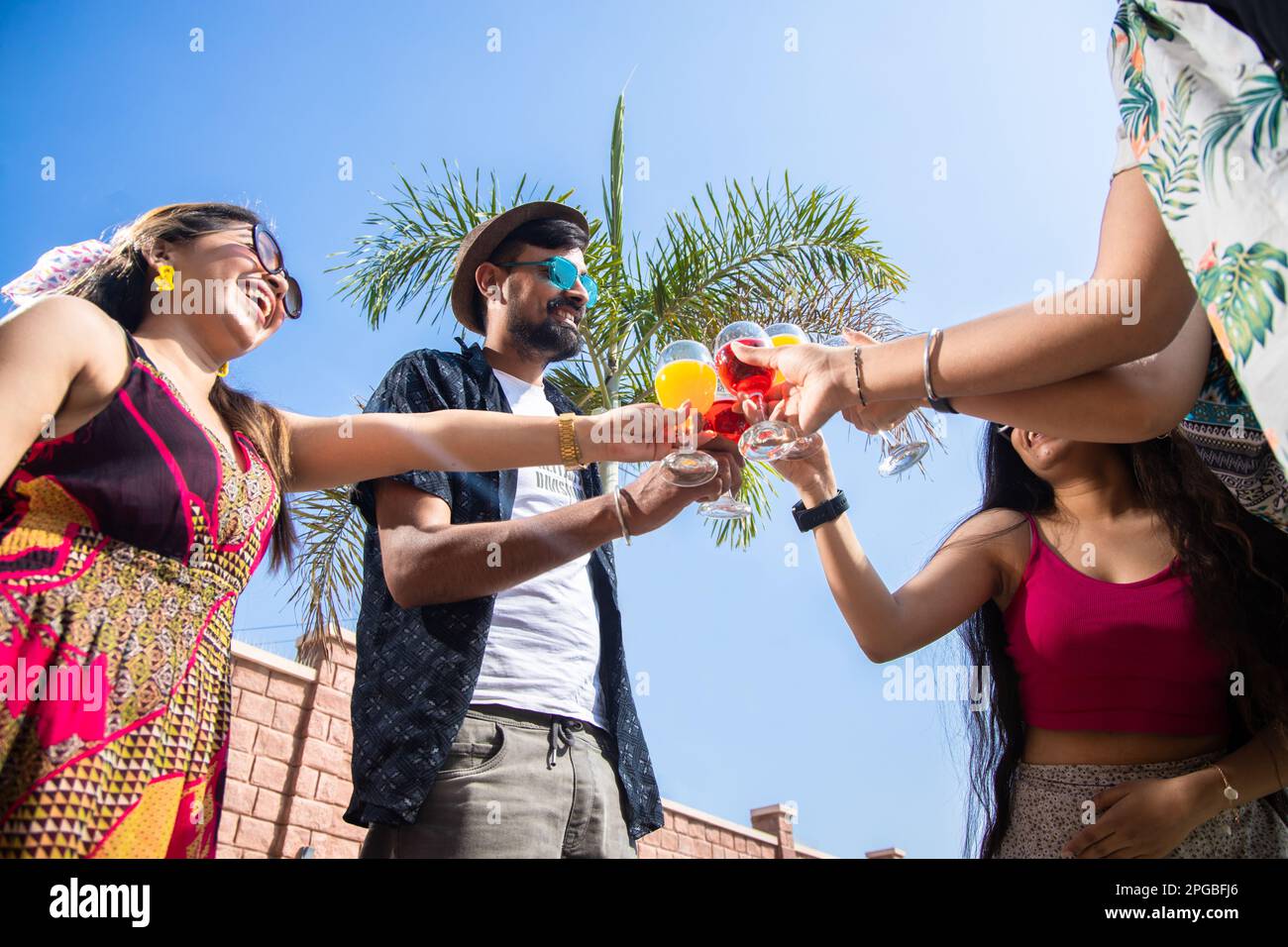 Indische Freunde, die zusammen Spaß haben, Cocktailgetränke anstoßen, Sommerparty feiern, junge Leute mit Gläsern, Toast mit frischem Saft. Schuss aus niedrigem Winkel. S Stockfoto