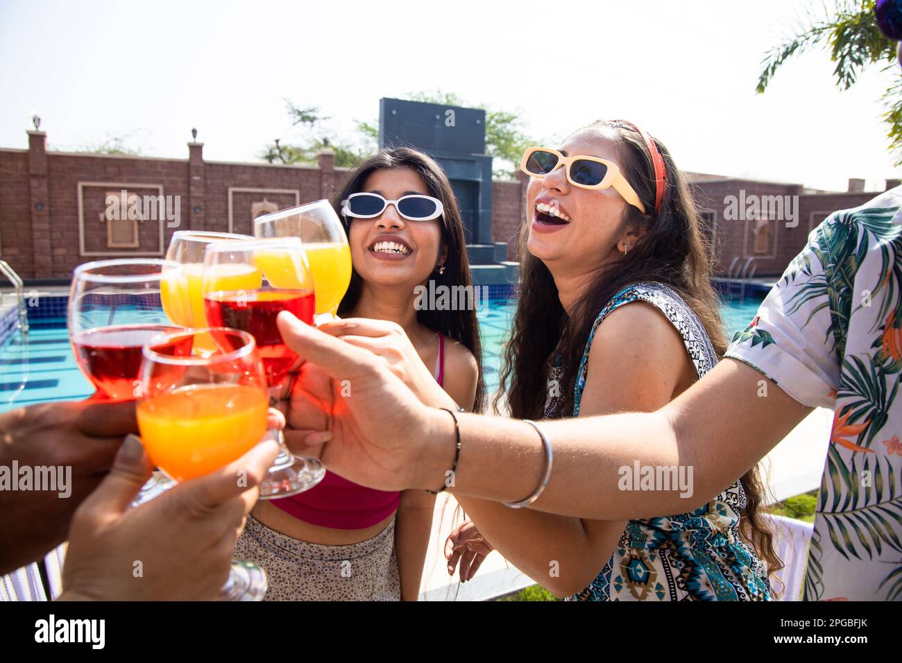 Junge indische Freundinnen, die eine Sonnenbrille tragen, zusammen Spaß haben, Cocktail-Drinks auf der Sommerparty toasten, wunderschöne brünette Mädchen, die Gläser klingeln Stockfoto