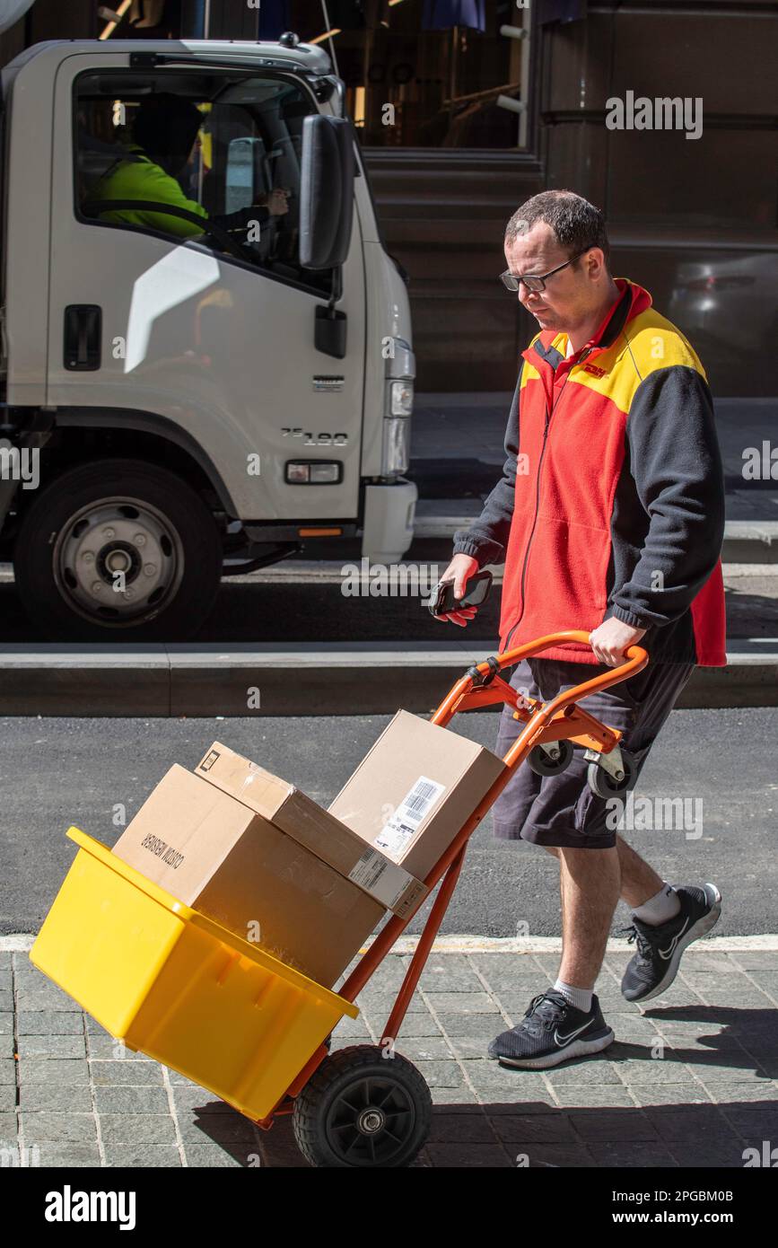 Ein DHL-Zusteller oder -Kurier, der Pakete mit einem zweirädrigen Transportwagen im Zentrum von Sydney, New South Wales, Australien transportiert Stockfoto