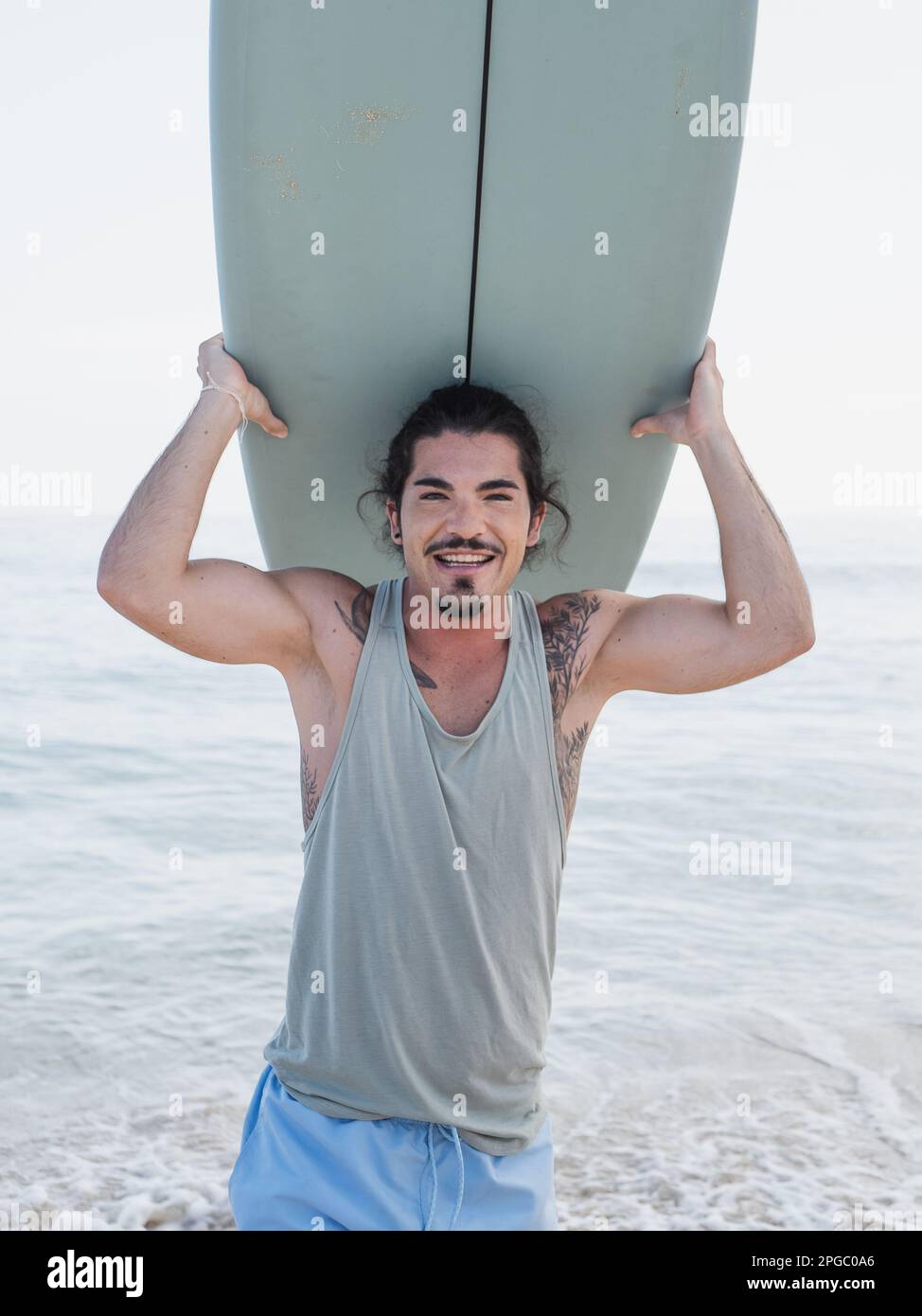 Porträt eines hispanischen Surfers am Meer mit seinem Surfbrett Stockfoto