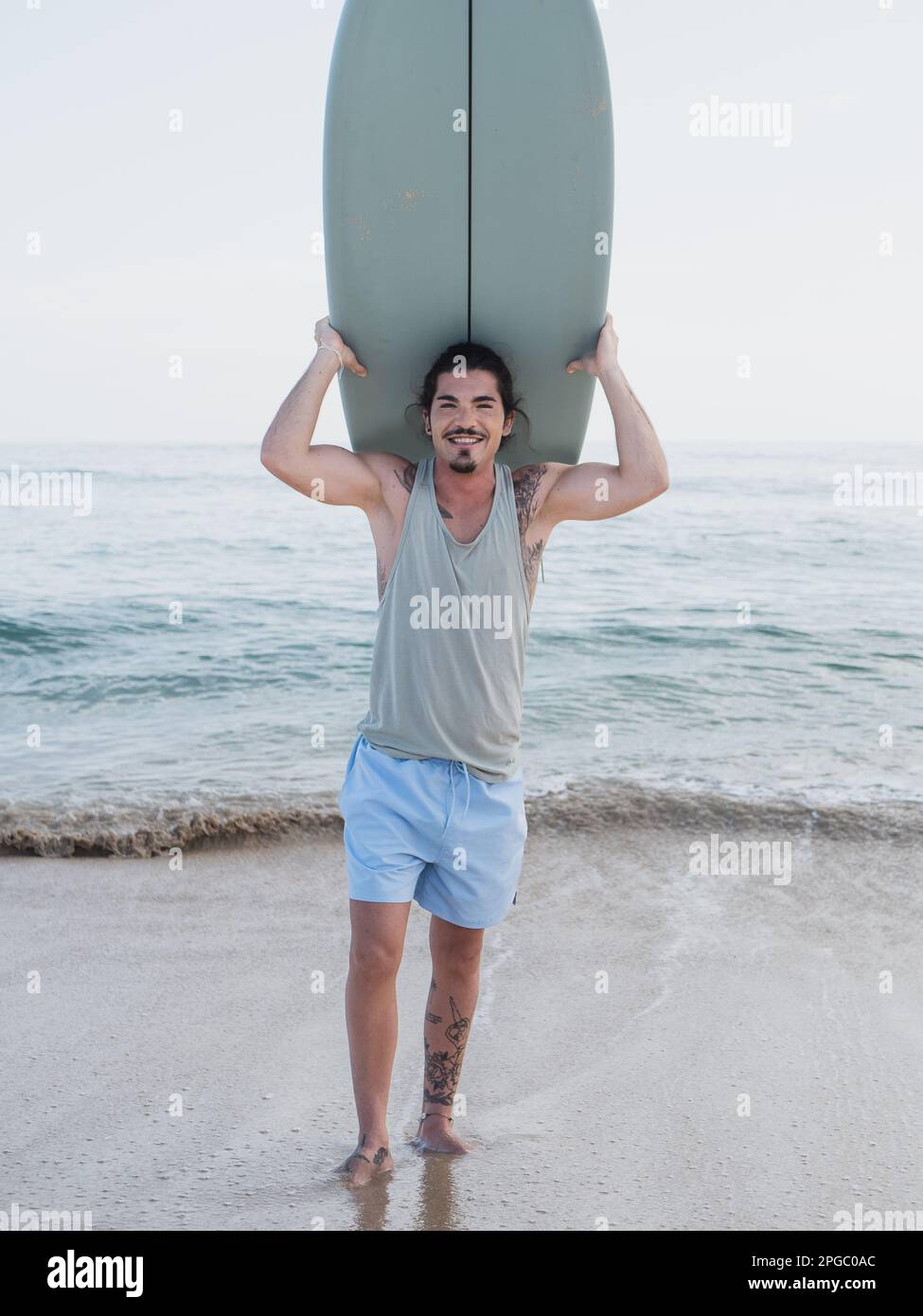 Hispanischer Surfer, der am Strand steht, lächelt und in die Kamera schaut Stockfoto