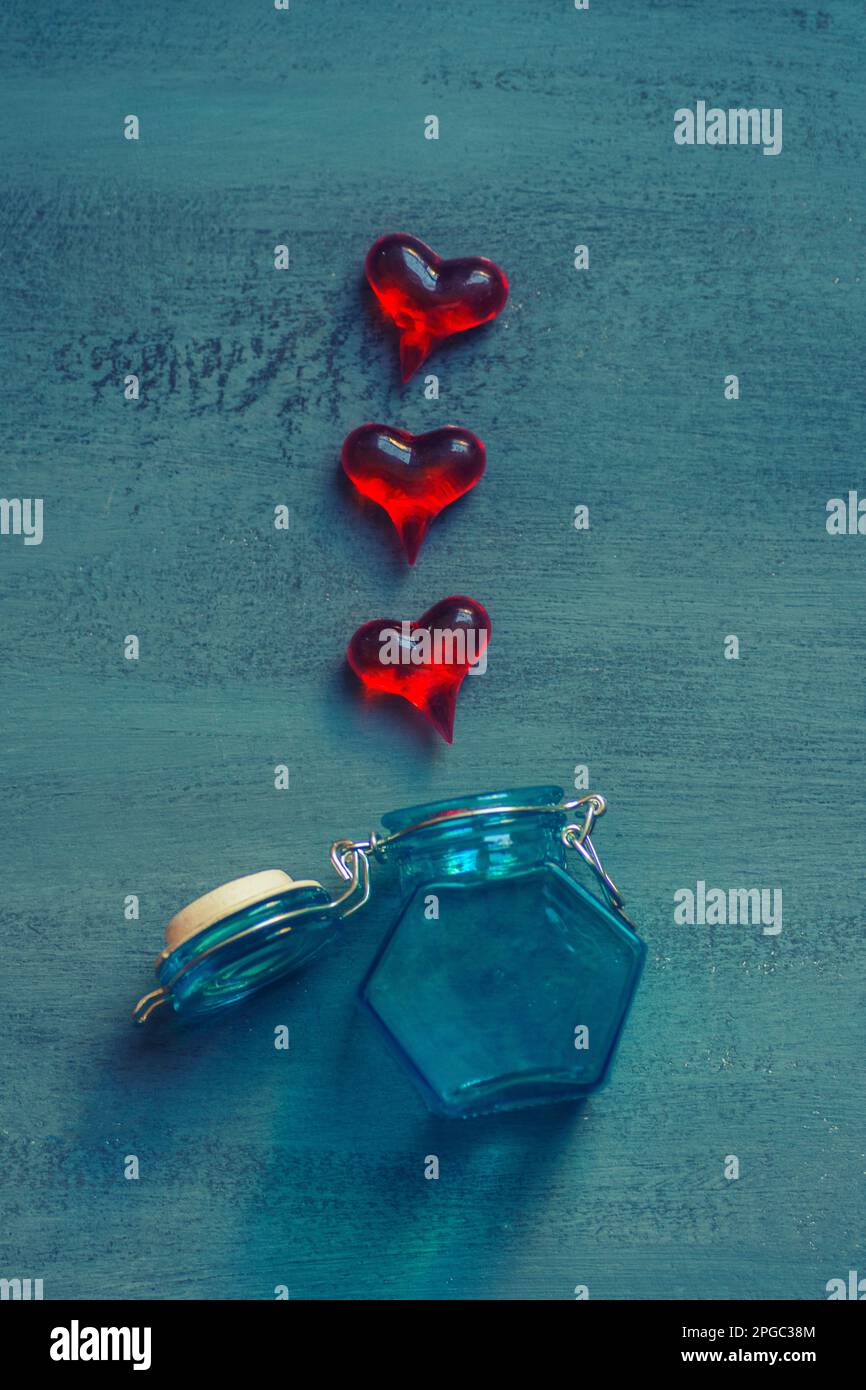 Drei rote Plattice-Herzen aus einem offenen blauen Glasgefäß Stockfoto