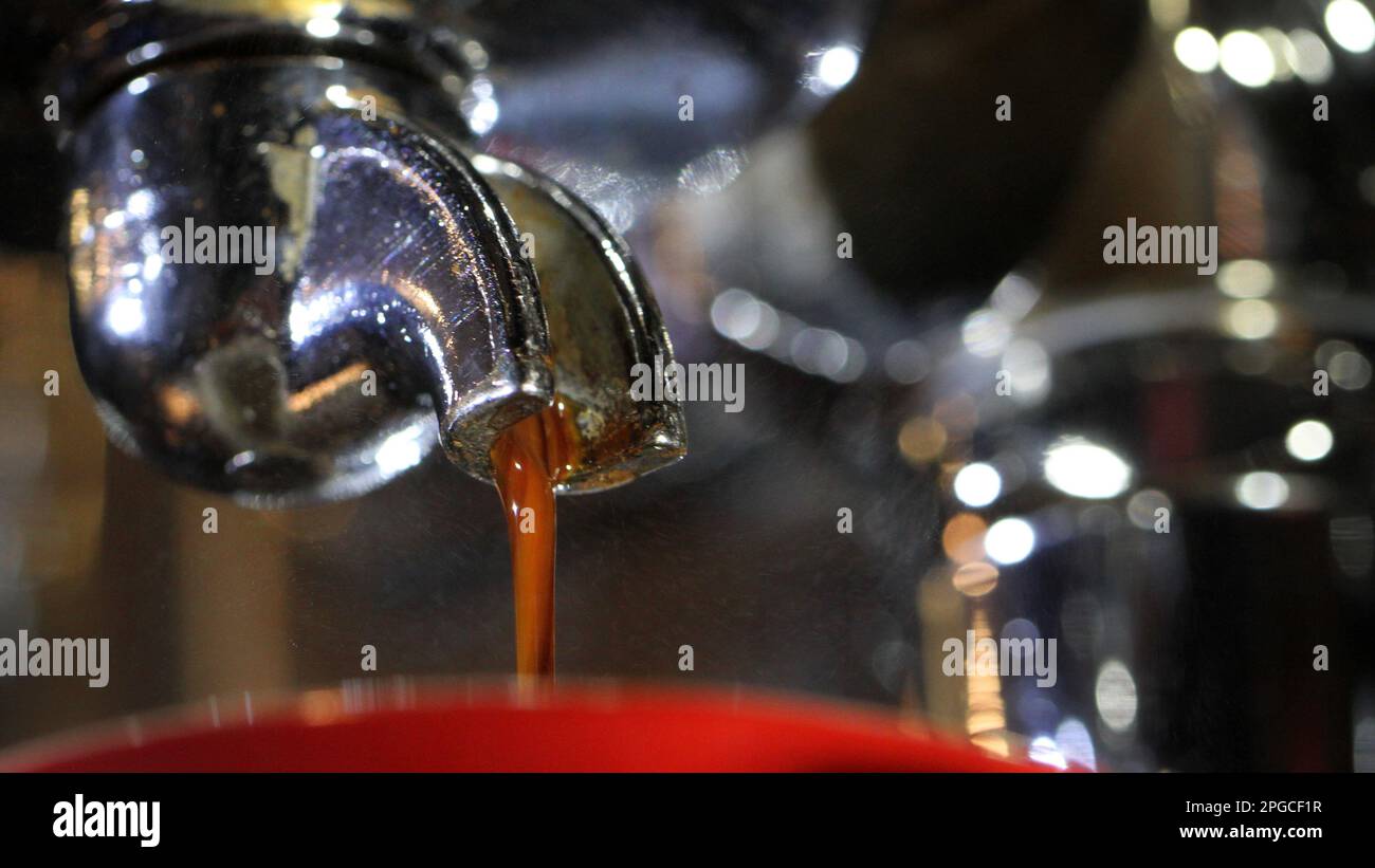 Isolierte Makronahaufnahme eines Espresso Shots, der aus einem Portafilter-Griff für Signalwörter in eine hellrote Tasse gegossen wird. Der Barista hat Kaffee zubereitet. Stockfoto