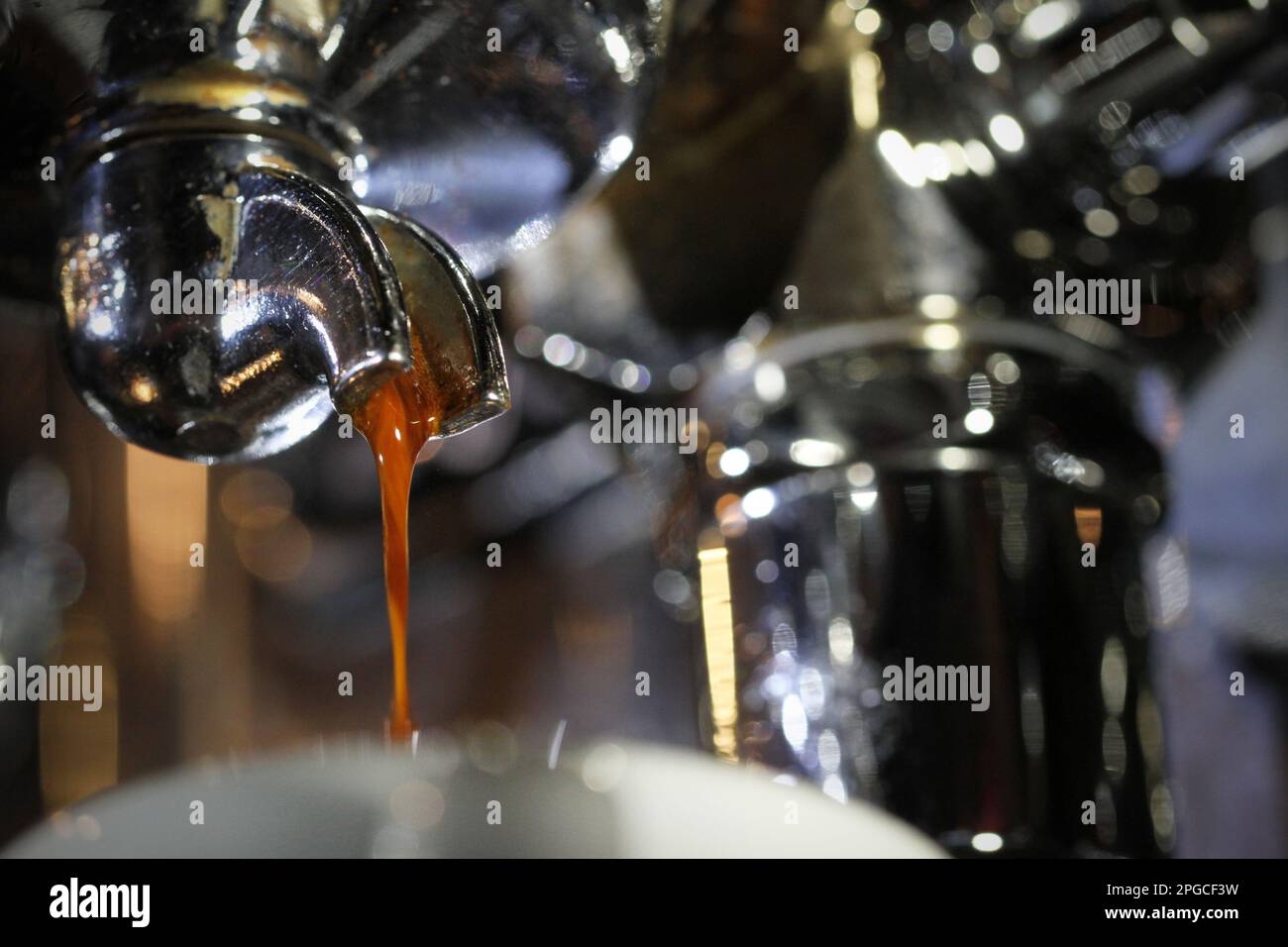 Extrem nahes Makrobild eines frischen, heißen Espressos, der in einem dünnen Strahl aus einem einzelnen Portafiltergriff einer Kaffeemaschine gegossen wird. Barista Stockfoto