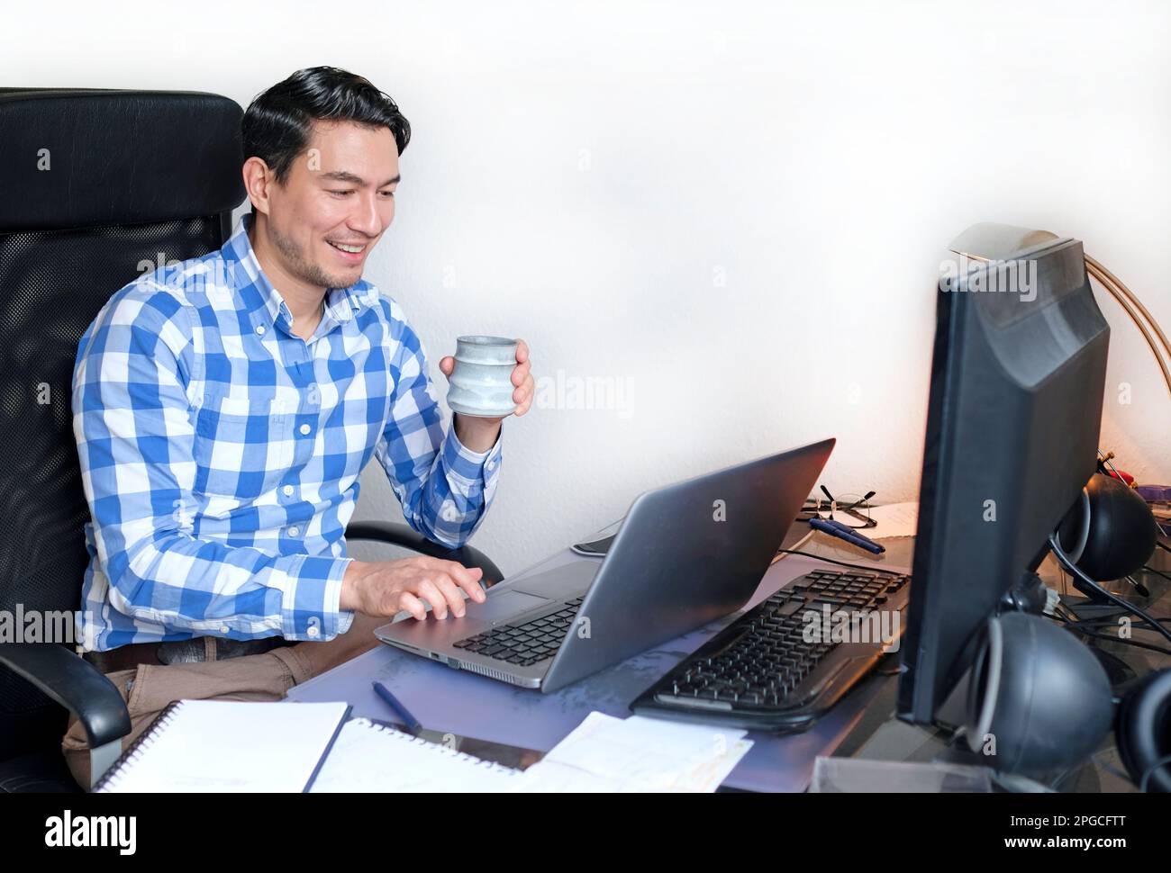 Ein Mann in einem karierten Hemd, der von zu Hause aus an einem Schreibtisch arbeitet Stockfoto
