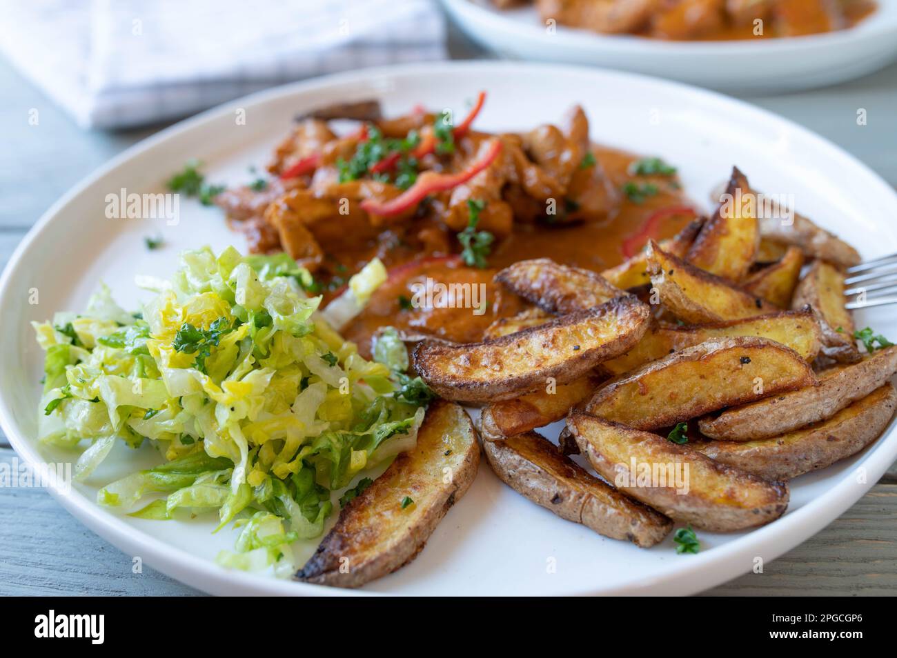 Kartoffelsplitter mit Hühnchen, Sauce und Salat auf einem Teller Stockfoto