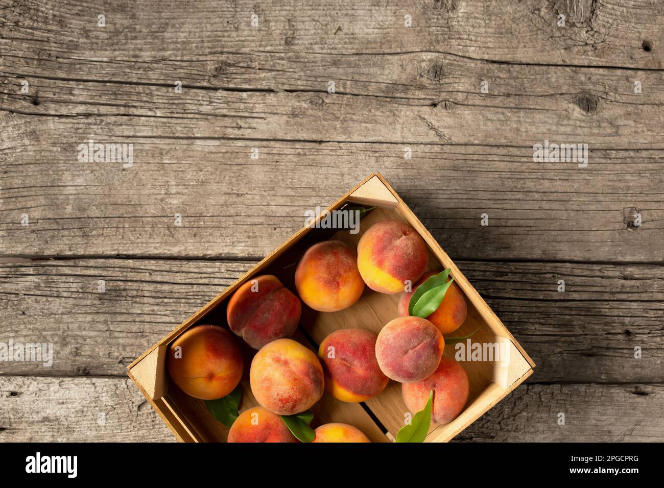 Pfirsiche in einer Schachtel auf einem hölzernen Hintergrund von oben. Frisches Obst auf klassischem Hintergrund. Pfirsiche auf Holzhintergrund. Sommerfrüchte in einer Holzbox. Stockfoto