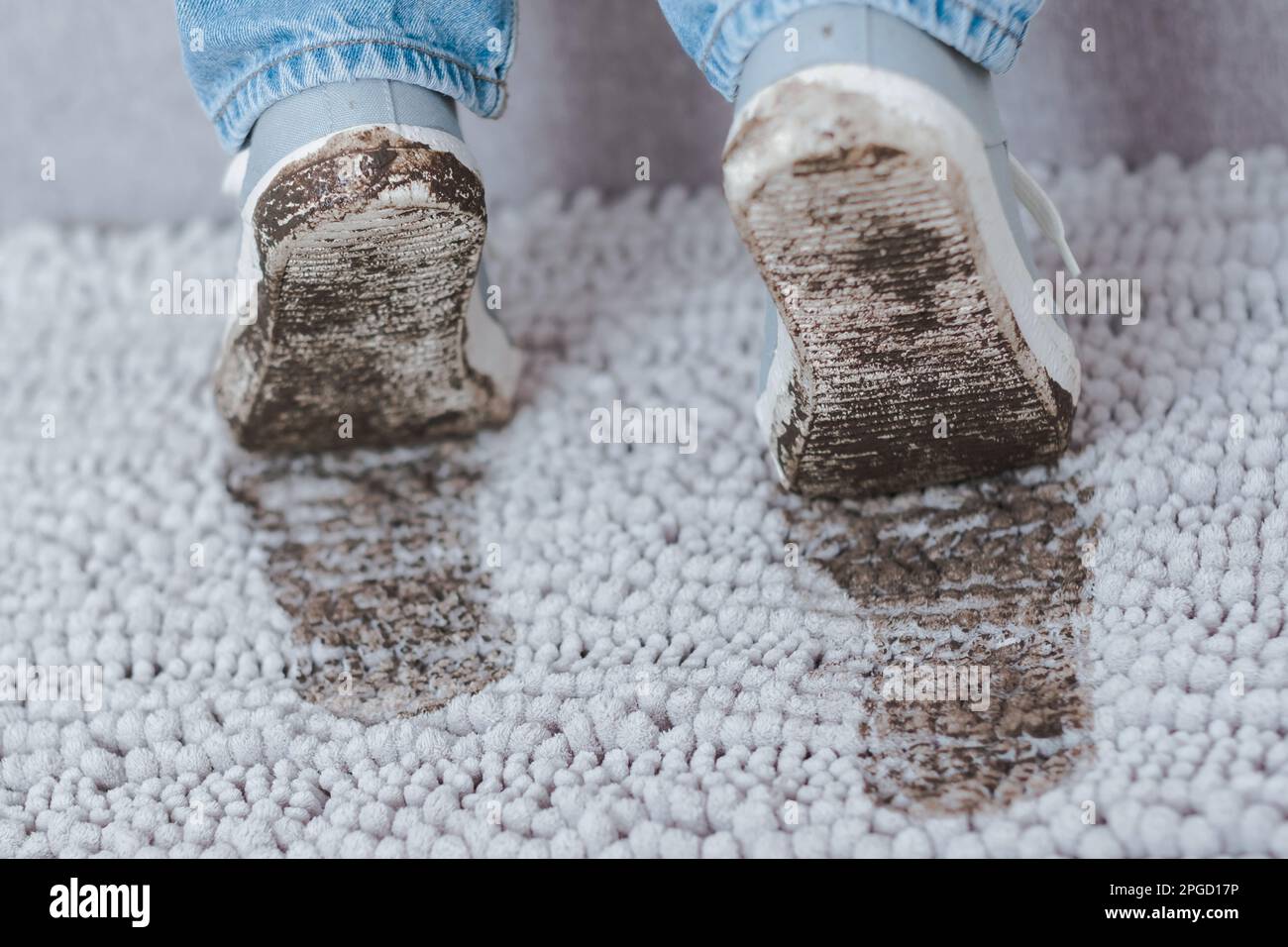 Schlammige Fußabdrücke auf grauem Teppich. Schmutzige Schuhe mit Schlamm und Erde. Täglich schmutziger Fleck. Stockfoto