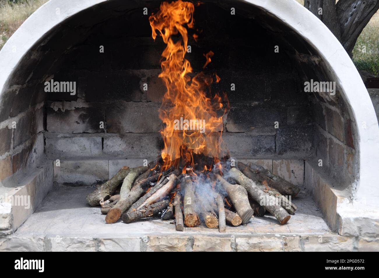 Gartenkamin mit einem Kamin, aus alten Ziegeln, mit einem Kamin drinnen. Ofen im Freien aus weißen Ziegeln mit einem Holzeimer Stockfoto