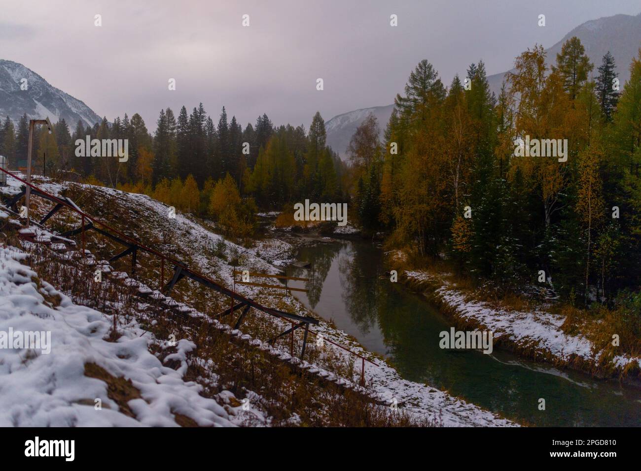 Die Treppen führen zu einem kleinen Fluss bei Nacht mit Nebel im Schnee der Herbstbäume im Altai-Gebirge. Stockfoto