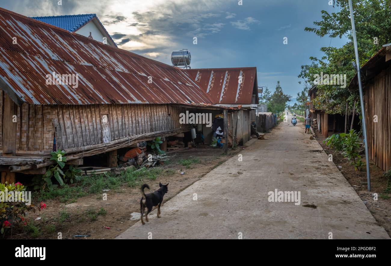 Eine Straße vorbei an einem traditionellen langen Haus auf Pfählen, das in das Mnong ethnische Minderheitendorf Buon Jun, Lien Son, Vietnam führt. Stockfoto