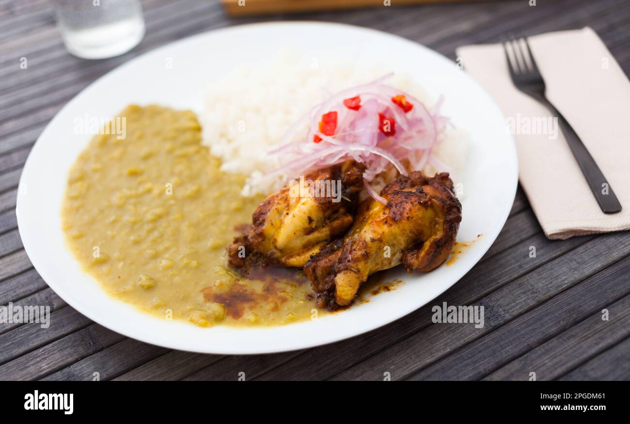 Hähnchenflügel mit pürierten Erbsen, Reis und eingelegten Zwiebeln auf weißem Teller Stockfoto