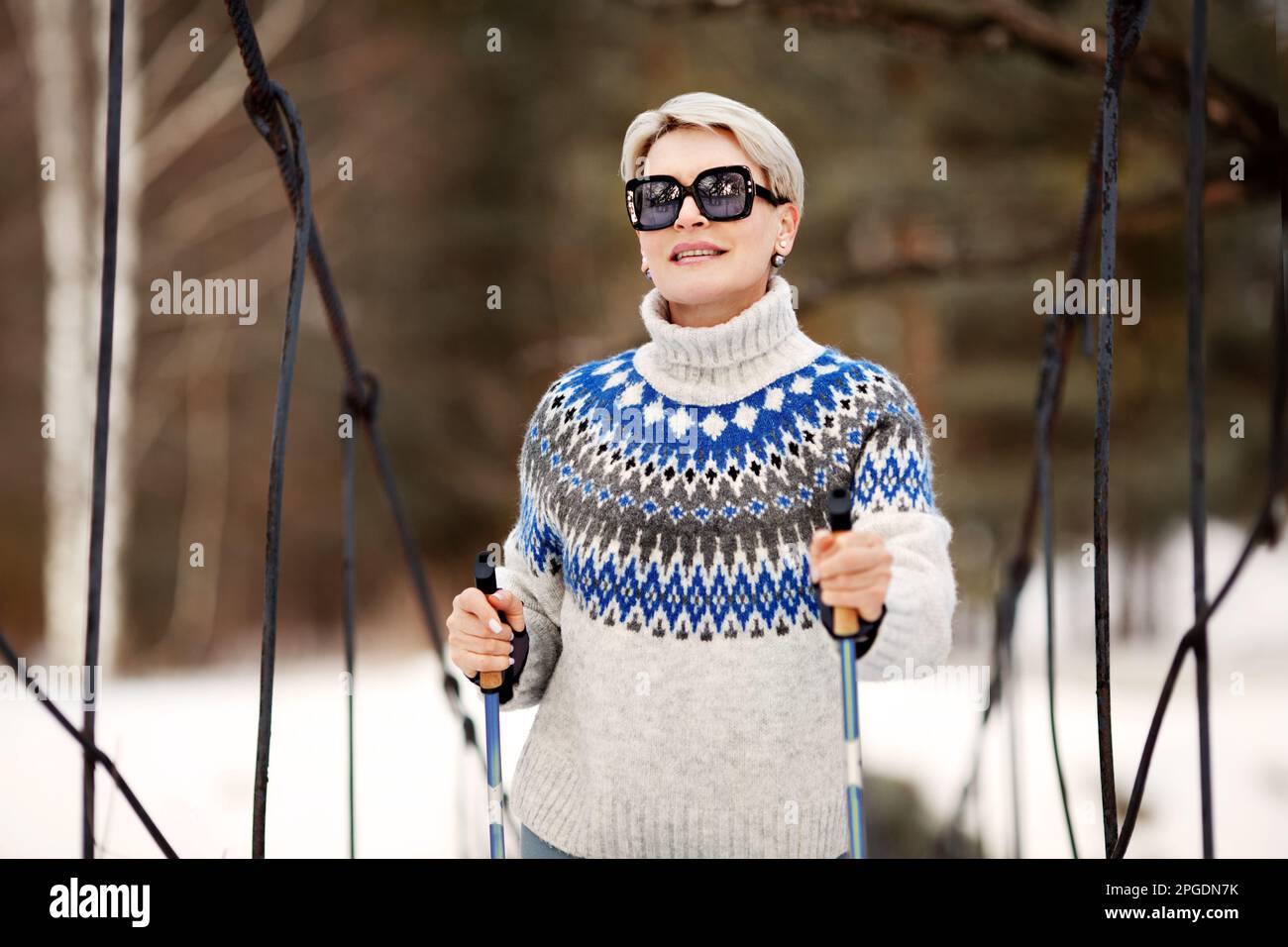Glückliche Frau, nordic, die mit Stöcken im Naturwald spaziert. Sportlicher, aktiver Lifestyle. Weibliches Modell im Außenporträt mit kurzen blonden Haaren in Sonnenbrille und Stockfoto