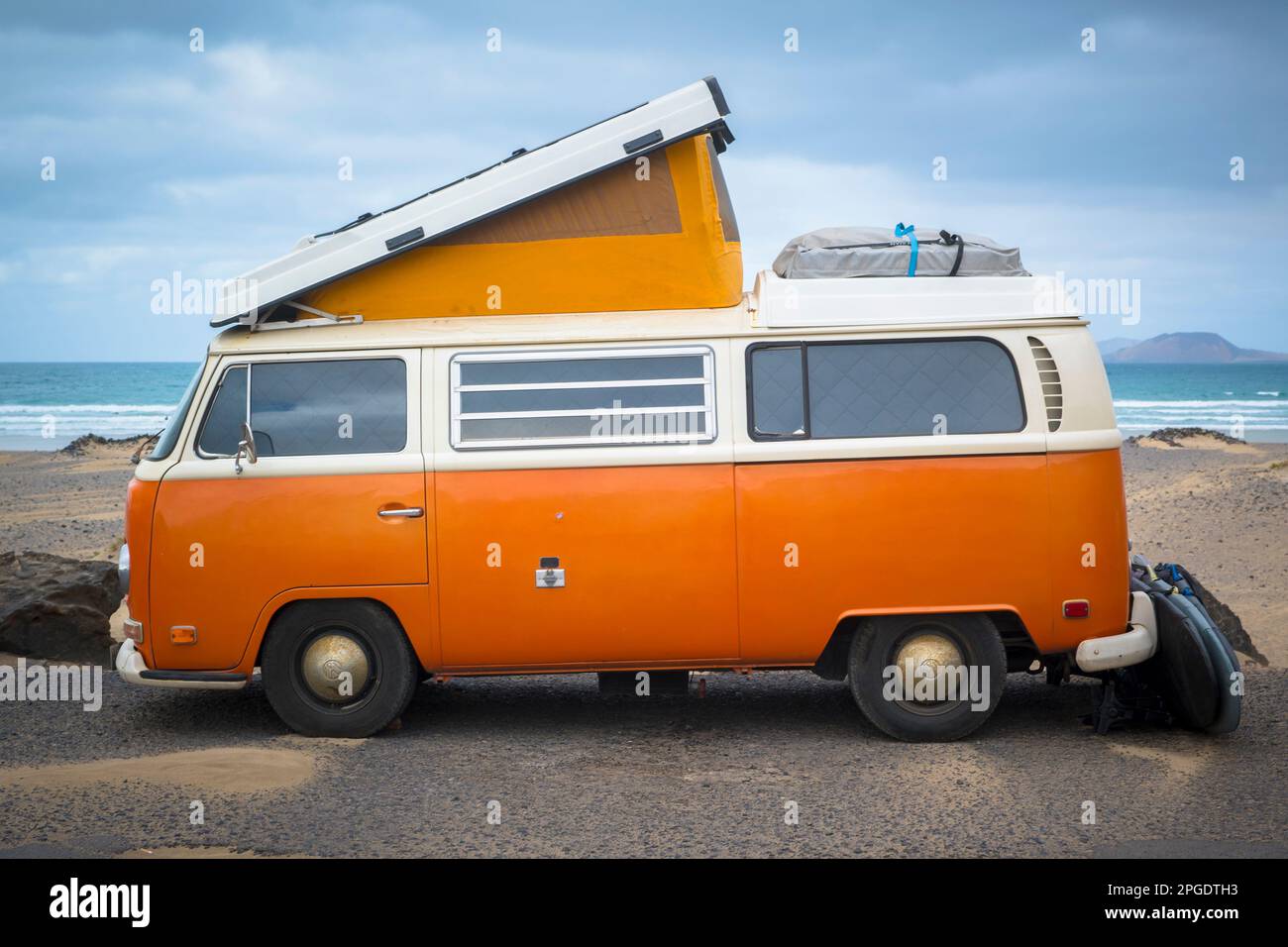 Famara, Lanzarote, März 2023, Illustrative Editorial: Blick auf den klassischen orangefarbenen Volkswagen T2 Wohnwagen am Strand Stockfoto