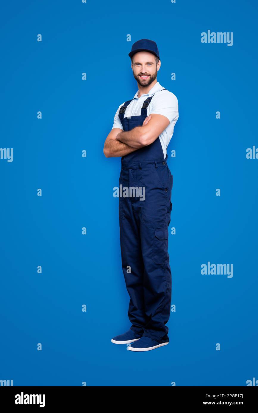 Vollkörperporträt in voller Größe, halbgedrehter fröhlicher Auftritt in blauer Uniform, die auf die Kamera schaut, mit gekreuzten Armen, isoliert auf grauem Hintergrund Stockfoto