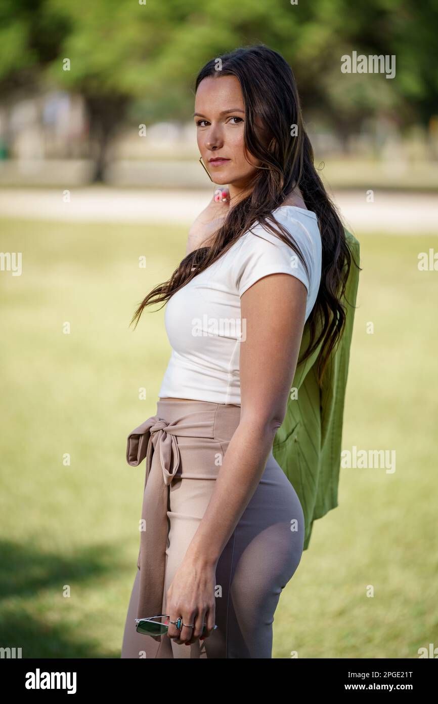 Foto einer wunderschönen jungen Frau Anfang 30s, die sich im Freien posiert, mit Jacke über dem Arm Stockfoto