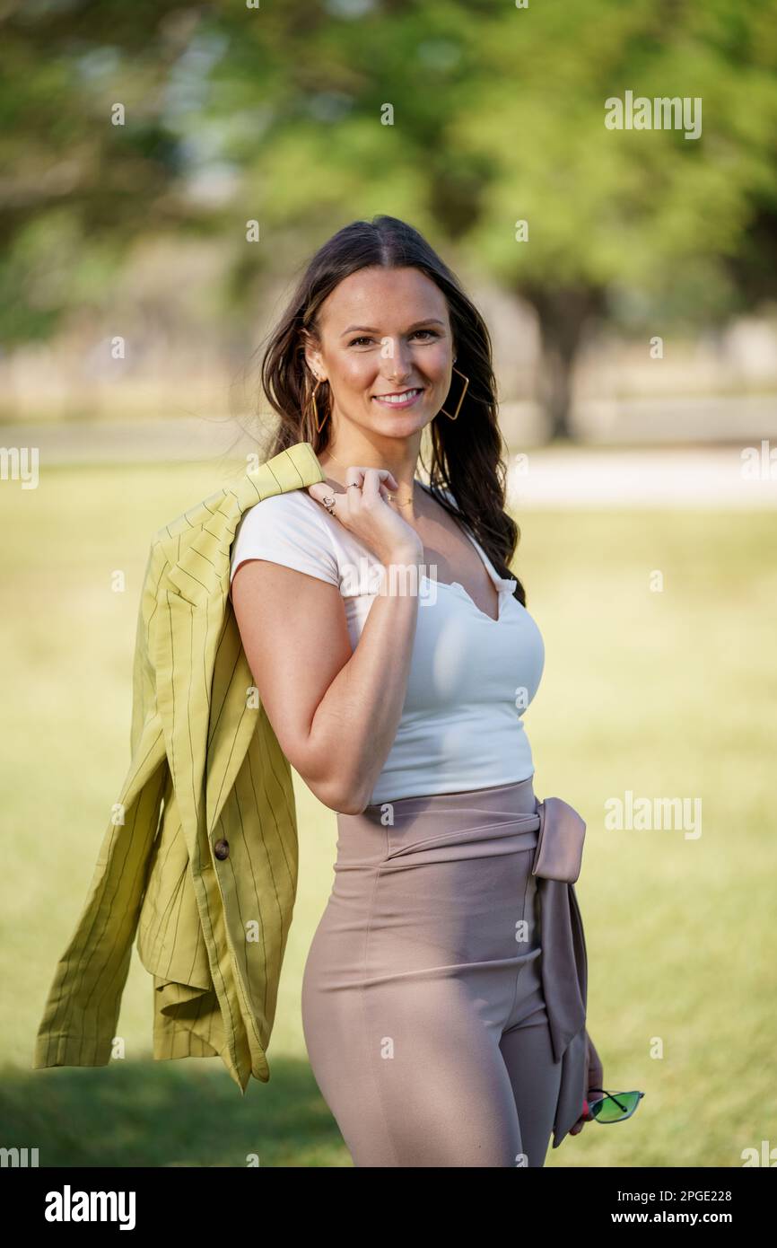 Foto einer wunderschönen jungen Frau Anfang 30s, die sich im Freien posiert, mit Jacke über dem Arm Stockfoto