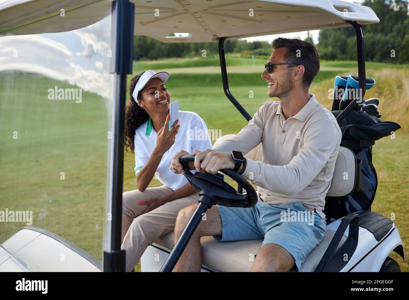 Porträt eines multiethnischen sportlichen Paares, das Fotos im Golfwagen im Freien macht und fröhlich lächelt Stockfoto