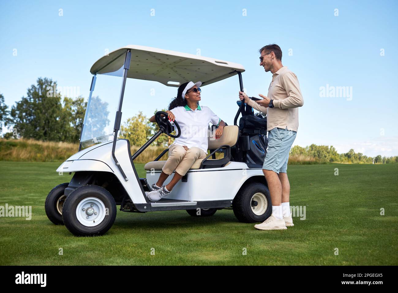 Porträt eines sportlichen jungen Paares, das sich auf dem Golfwagen draußen im Green Field unterhält Stockfoto