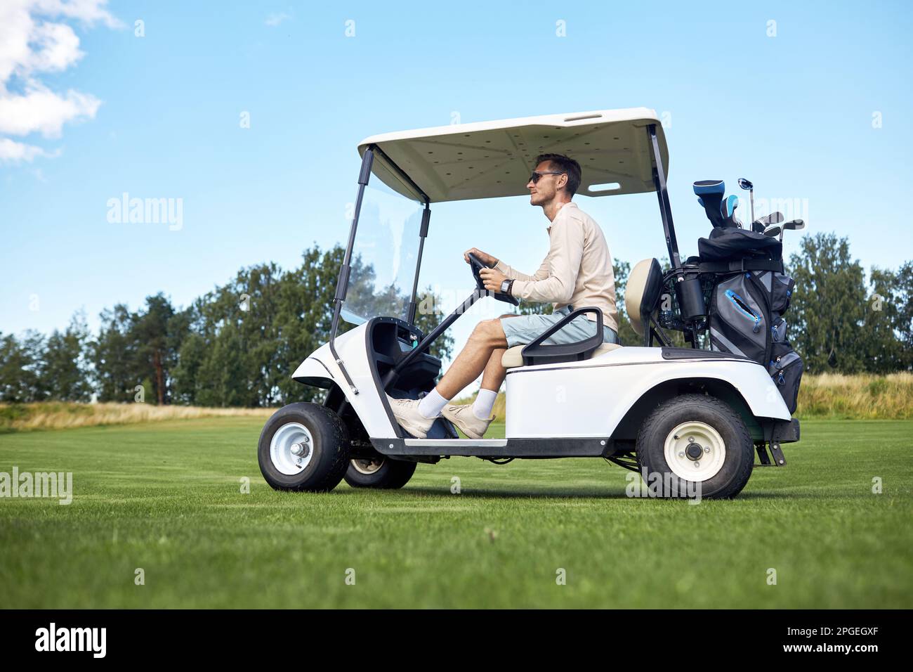 Durchgehende Seitenansicht eines Mannes, der einen Golfwagen über das grüne Feld im Sportclub fährt, Kopierbereich Stockfoto