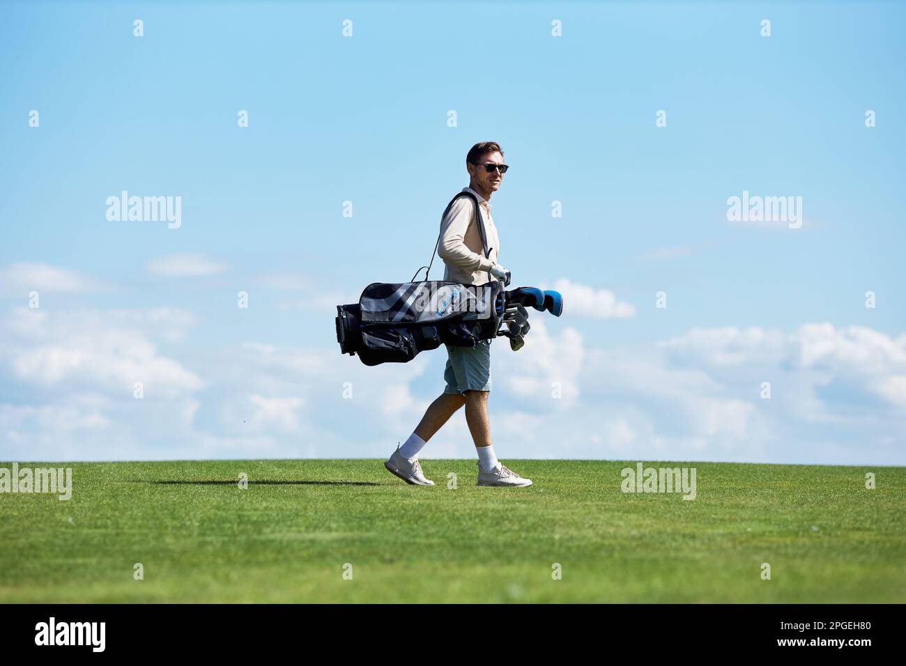 Minimales seitliches Porträt eines reichen, sportlichen Mannes mit Golftasche, der auf dem grünen Feld gegen den Himmel läuft, Kopierraum Stockfoto