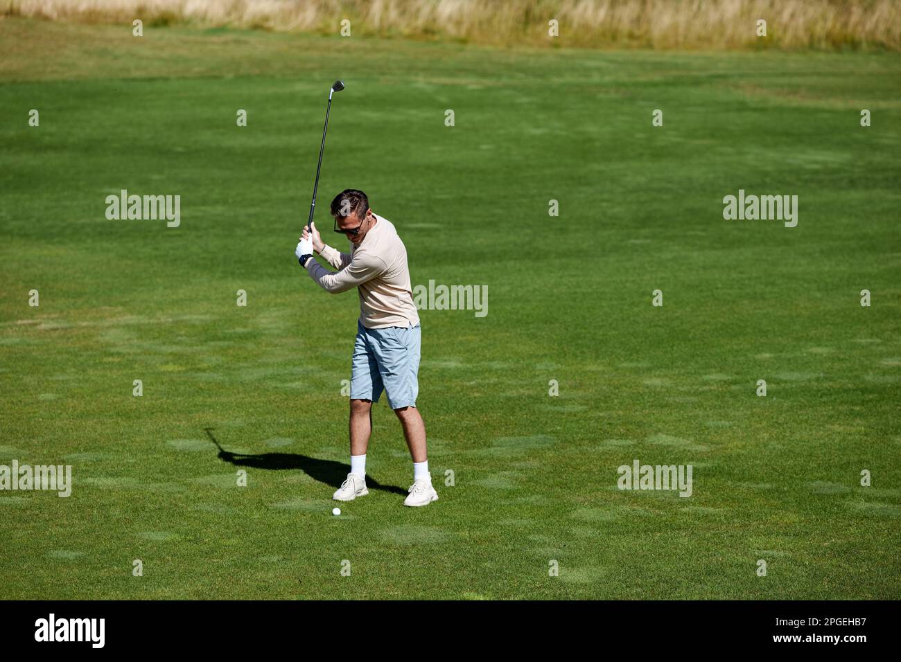 Blick aus einem hohen Winkel auf einen sportlichen Mann, der Golf auf dem grünen Feld spielt und einen Schaukelgolfclub mit Präzision, Kopierbereich Stockfoto