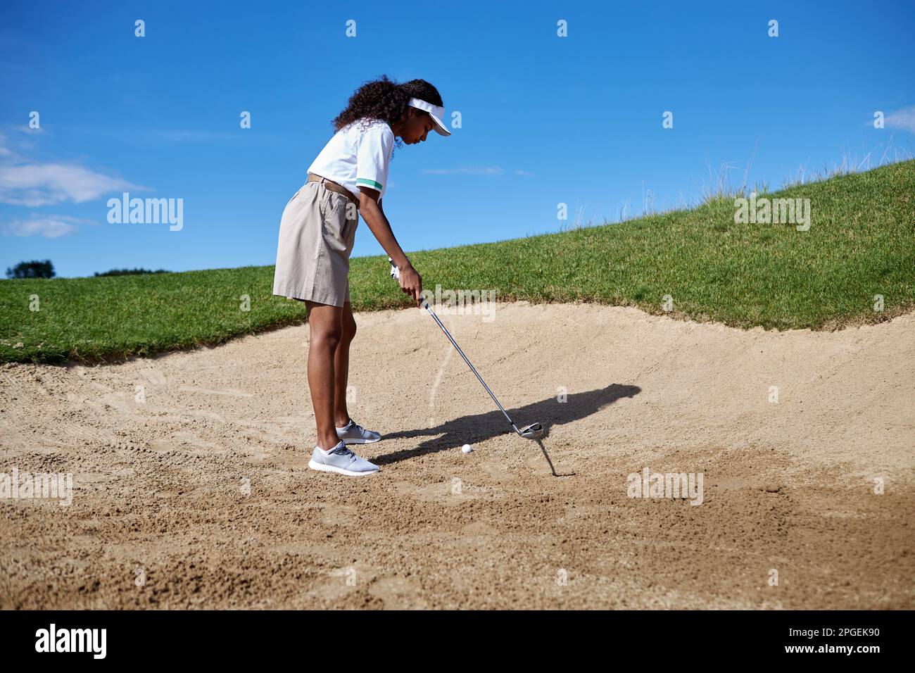 Ein langes Porträt einer schwarzen jungen Frau, die draußen Golf spielt, im Sandkasten steht und zielt Stockfoto