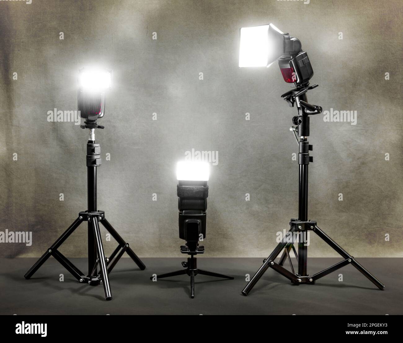 Horizontale Aufnahme von drei funkgesteuerten Blitzlichtern, die auf einen Leinenhintergrund schießen. Stockfoto