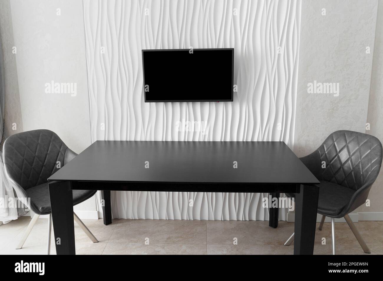 Minimalistisches Interieur. Ein großer Glastisch mit Stühlen an einer weißen Wand mit einem Fernseher in der Mitte. Küchendesign. Dinner-Zone Stockfoto