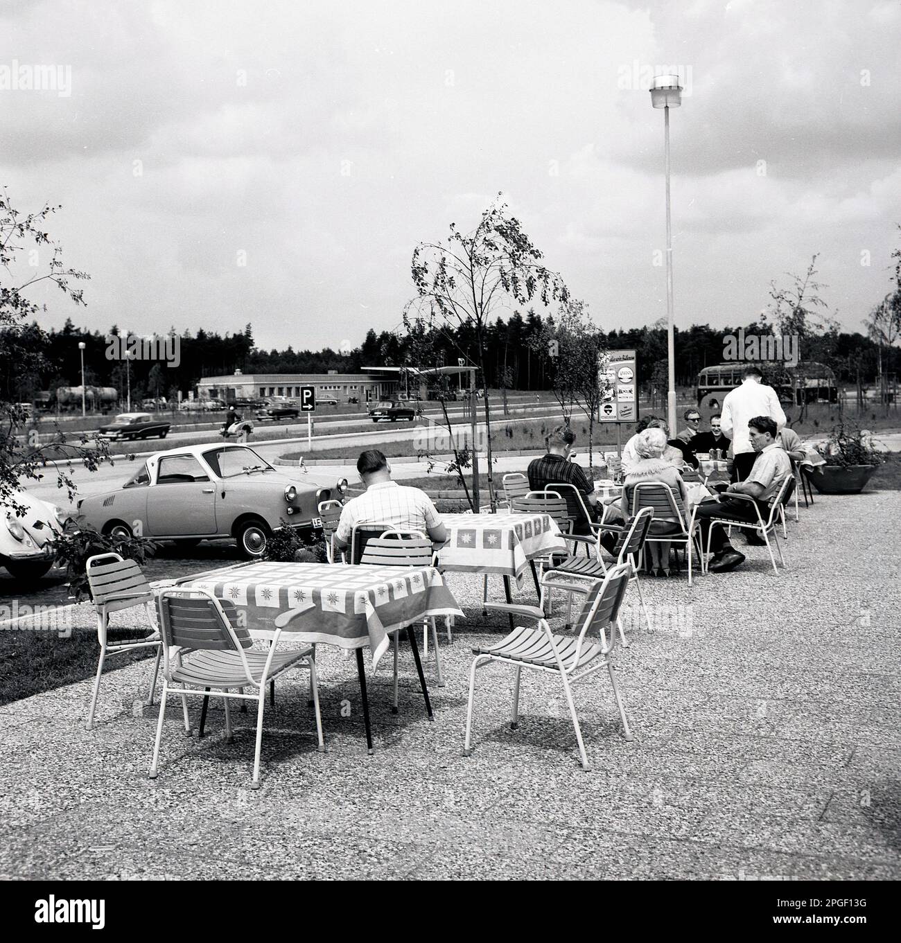 1960er, historisch, Leute sitzen draußen auf einem Terrassenbereich an einer Autofahrt-Raststätte und Erfrischungsstation - mit Kellnertischservice - neben einer Straße oder Autobahn, Deutschland. Stockfoto