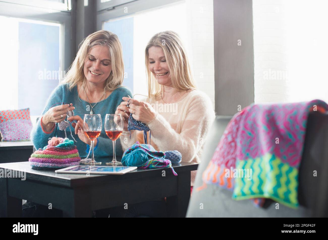 Zwei Frauen stricken Schalldämpfer und trinken Wein im Café und lächeln, Bayern, Deutschland Stockfoto
