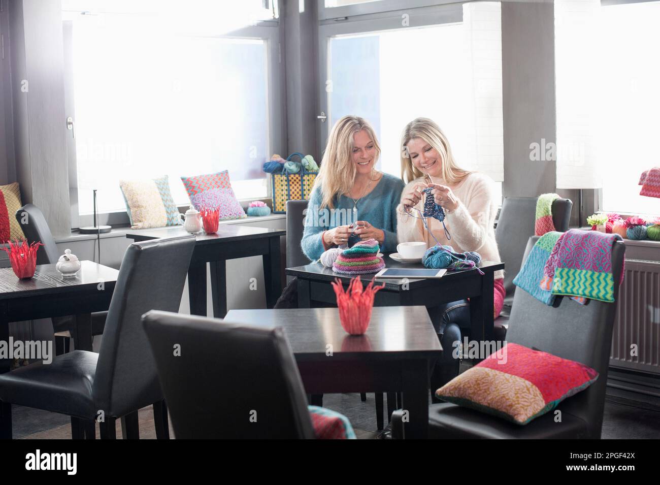 Zwei Frauen stricken Schalldämpfer und trinken Kaffee im Café und lächeln, Bayern, Deutschland Stockfoto