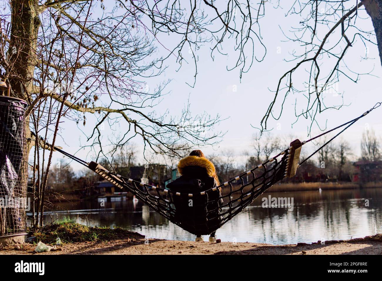 Person, die in einer Hängematte sitzt und an zwei Bäumen am Fluss hängt Stockfoto