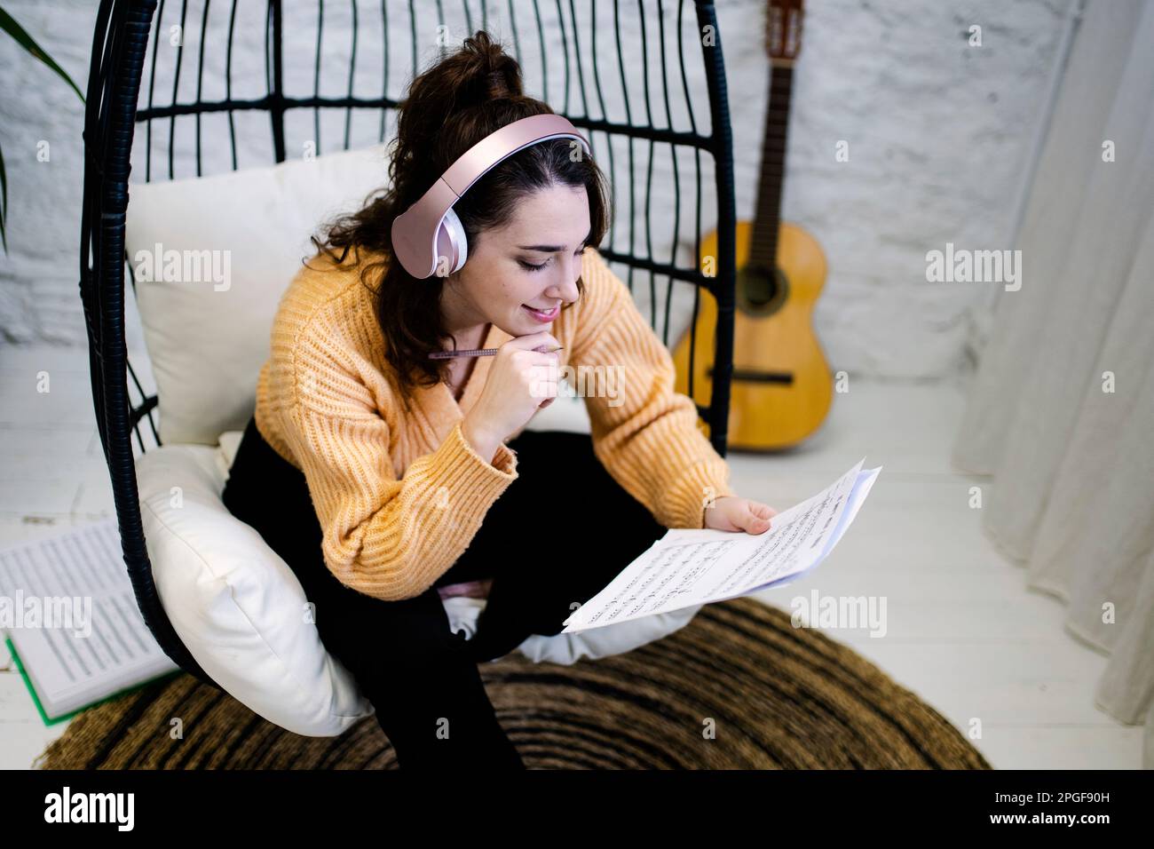 Junge Frau mit Kopfhörern und einer Gitarre, die zu Hause Musik komponiert Stockfoto