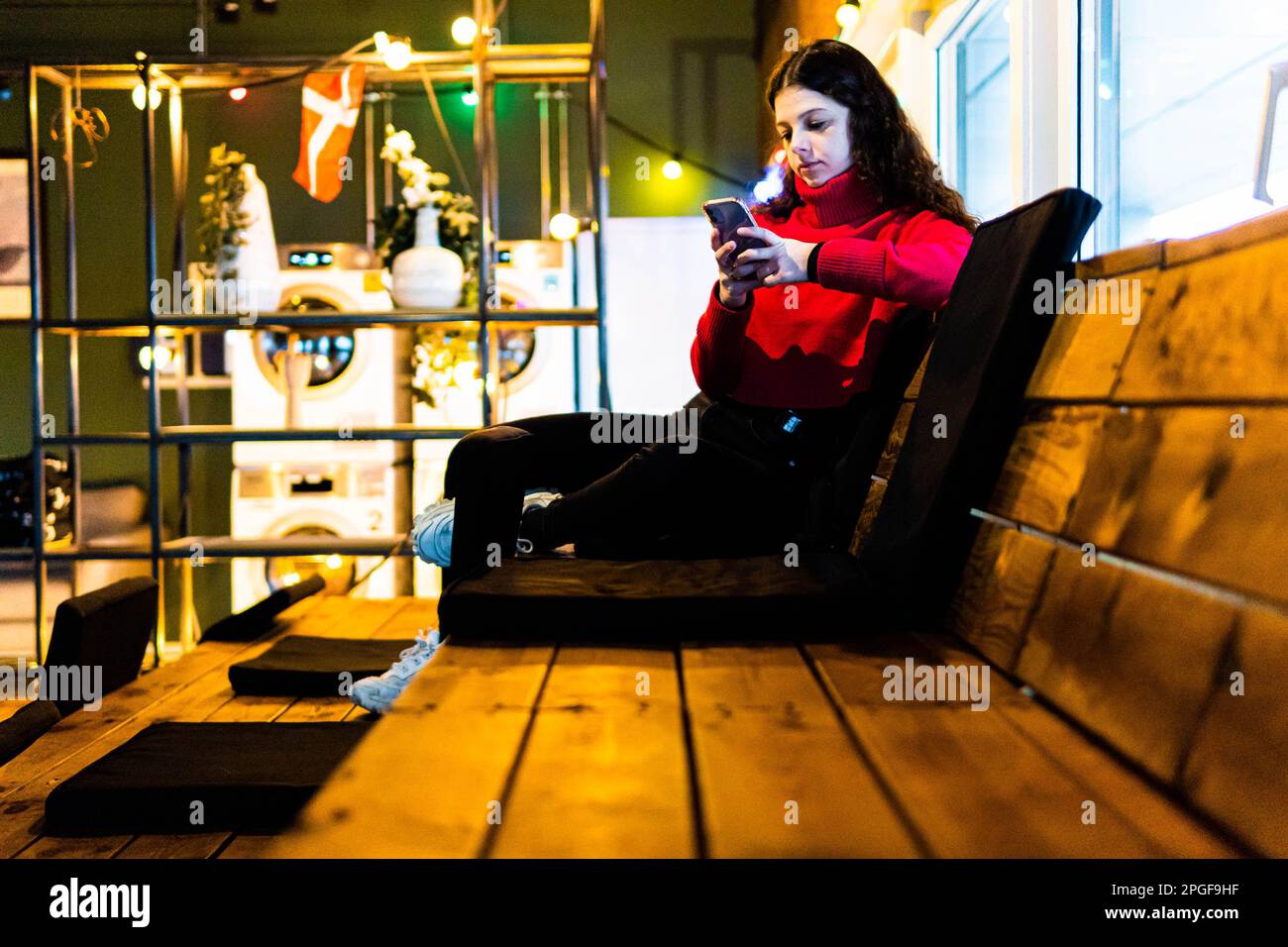 Eine Frau, die auf Holzbänken in einem Hotel sitzt und auf das Handy schaut Stockfoto
