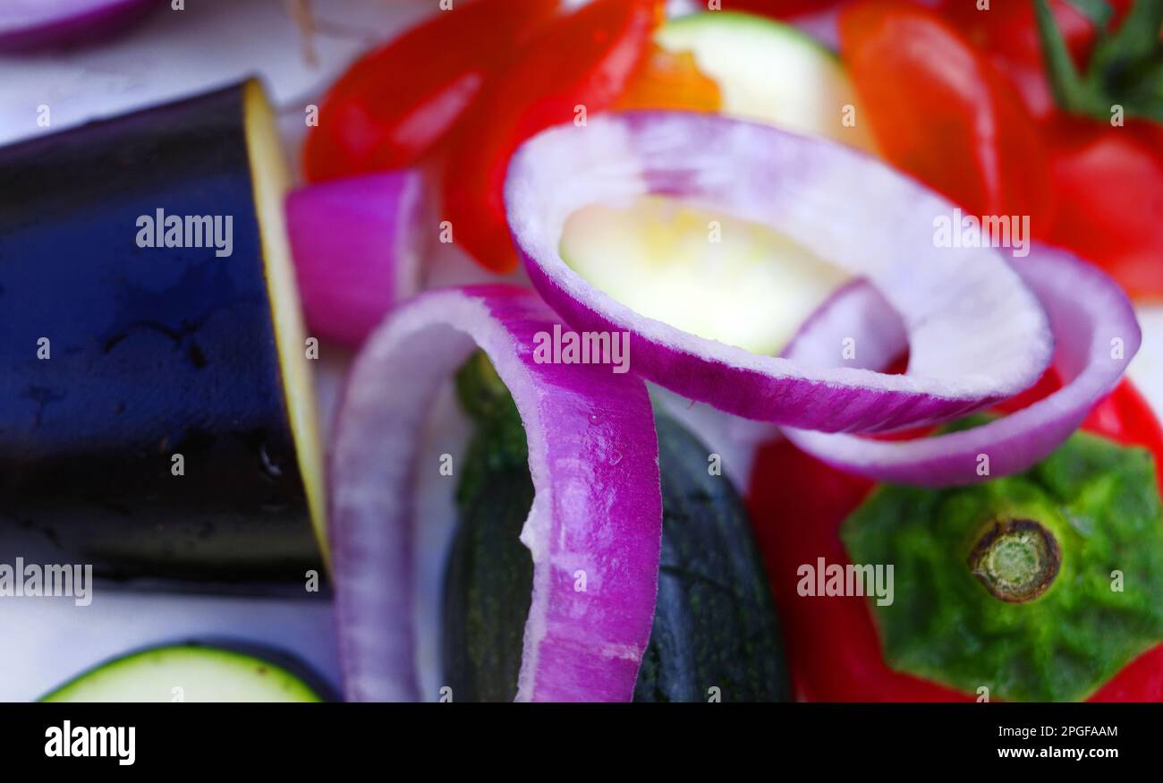 Gemischtes Gemüse für ein mediterranes Gericht auf einem weißen Schneidebrett. Rote Zwiebeln, Zucchini, Aubergine, Tomaten und Paprika sind auf dem Teller. Ein Stockfoto