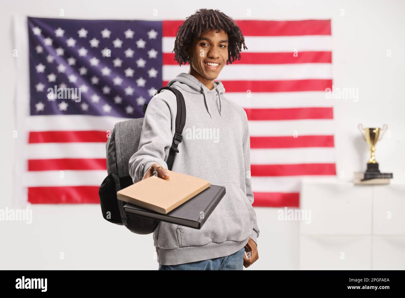 afroamerikanischer Student mit Rucksack, der Bücher vor einer US-Flagge ausgibt Stockfoto