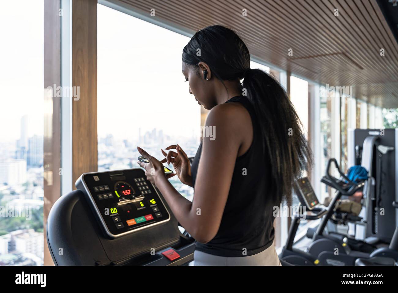 Schwarze Frau, die auf einem Laufband im Fitnessstudio läuft und mit ihrem Handy spricht Stockfoto